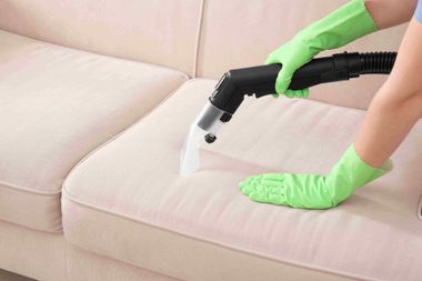 Green-gloved hands steam-cleaning a beige sofa cushion
