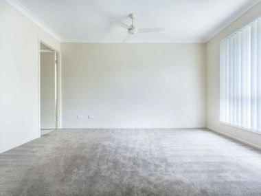 Empty beige bedroom with carpet, ceiling fan, and vertical blinds on the right wall