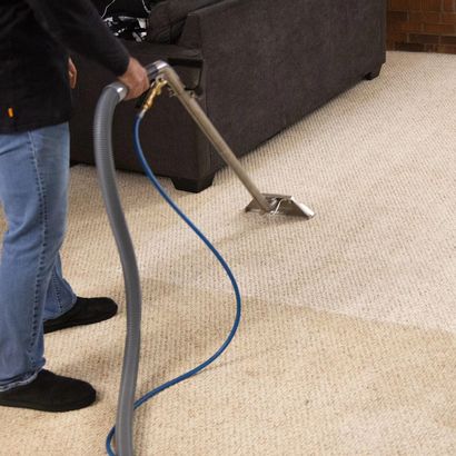 Person cleaning a beige carpet with a vacuum hose near a dark sofa