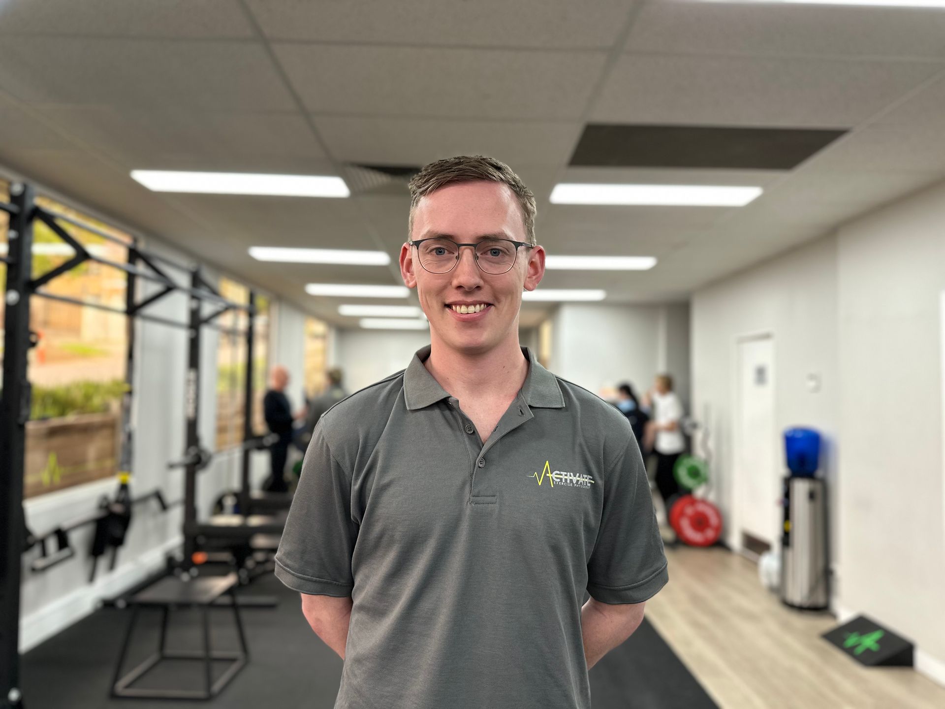 A man wearing glasses and a grey shirt is standing in a gym.