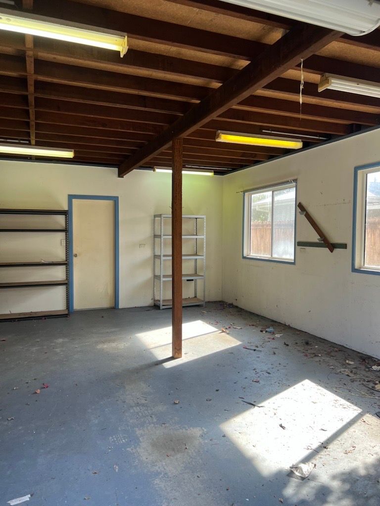 Interior of a garage with a concrete floor, shelves, windows, and exposed ceiling beams. A central wooden pole supports the ceiling — Rob's Rubbish Removal in Byron Bay, NSW