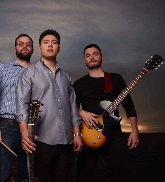 Three men standing next to each other holding guitars