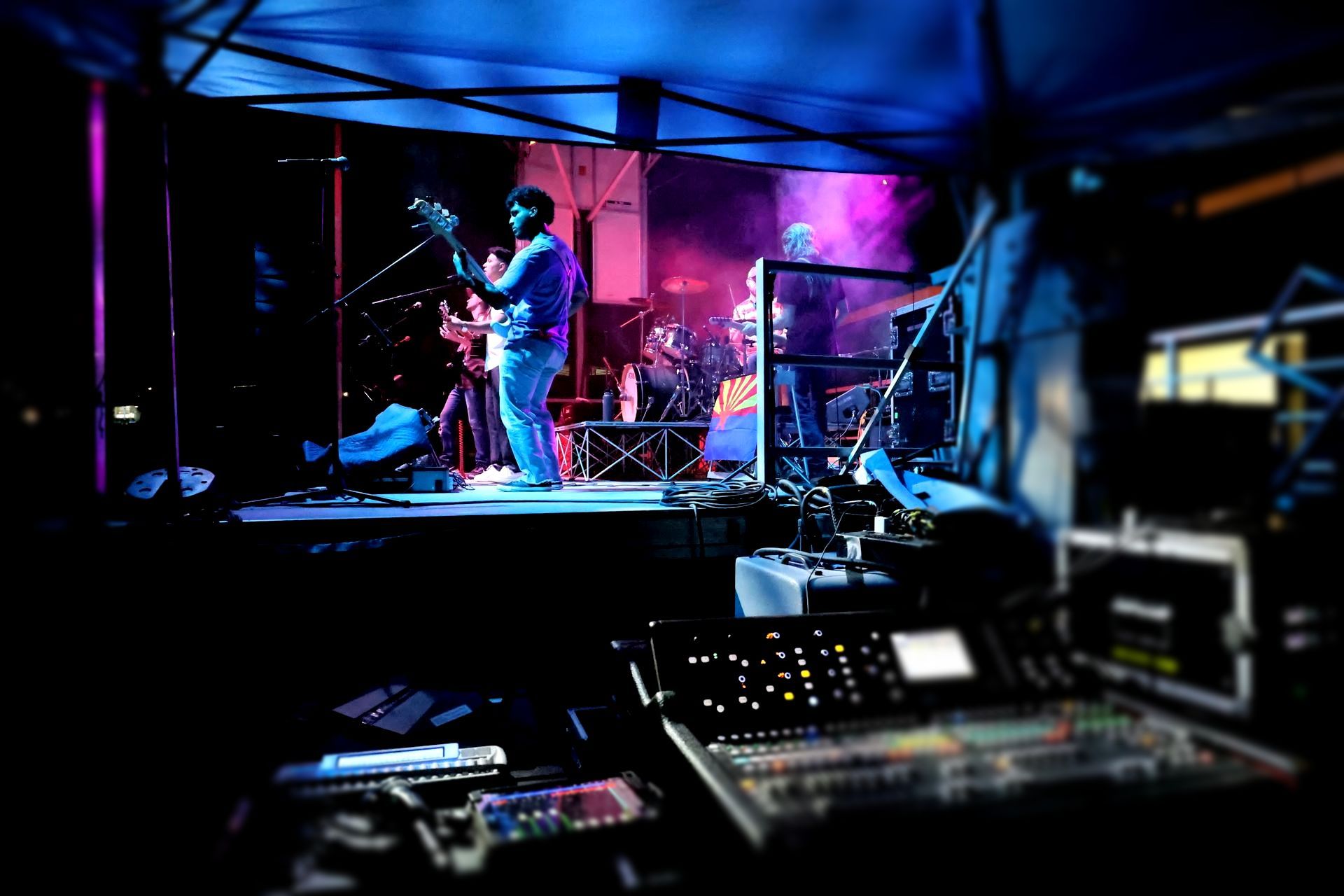 A blurry picture of a band on stage with a mixer in the foreground