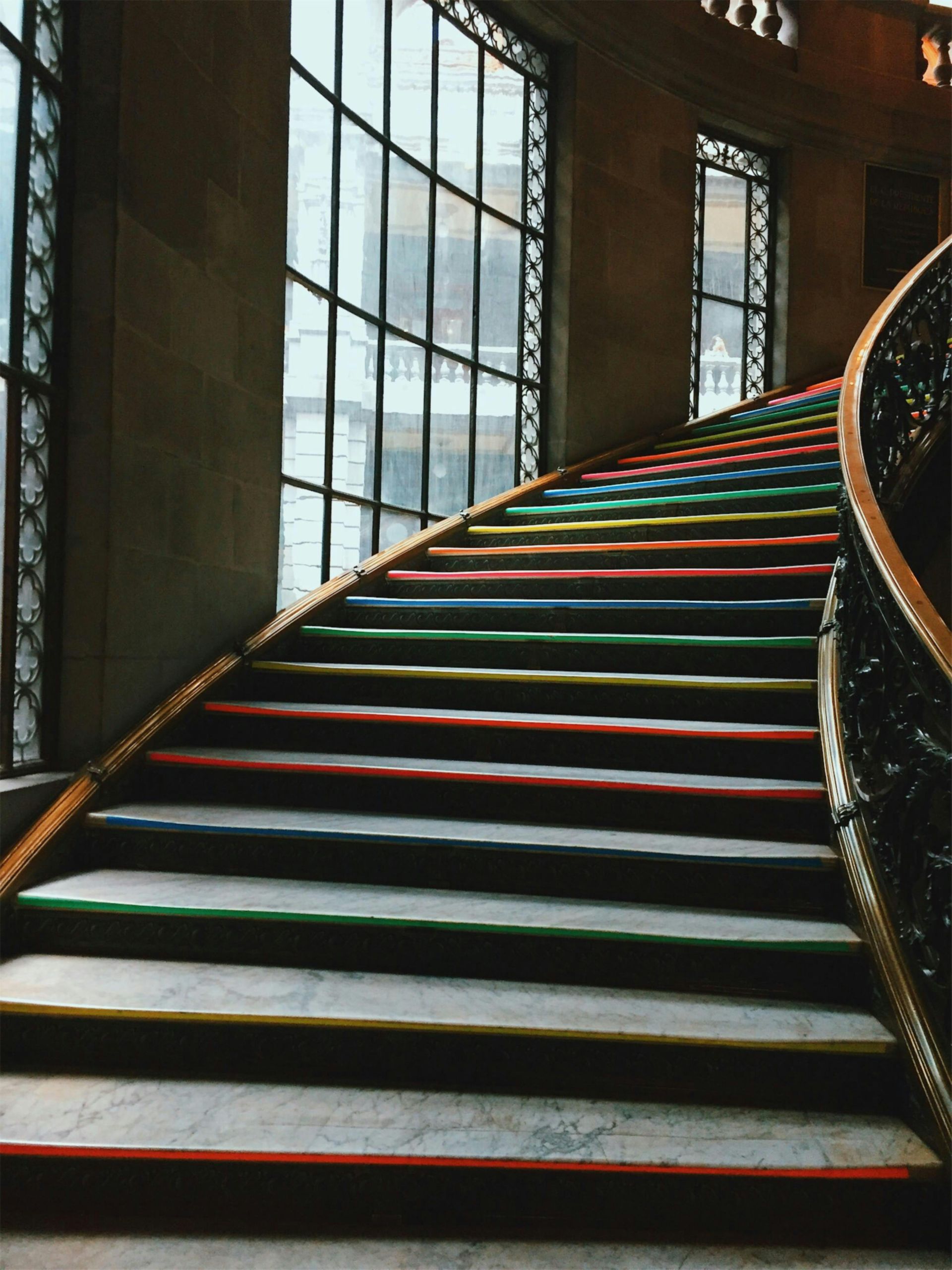 Curved staircase with brightly colored treads: red, orange, yellow, green, blue, and black.