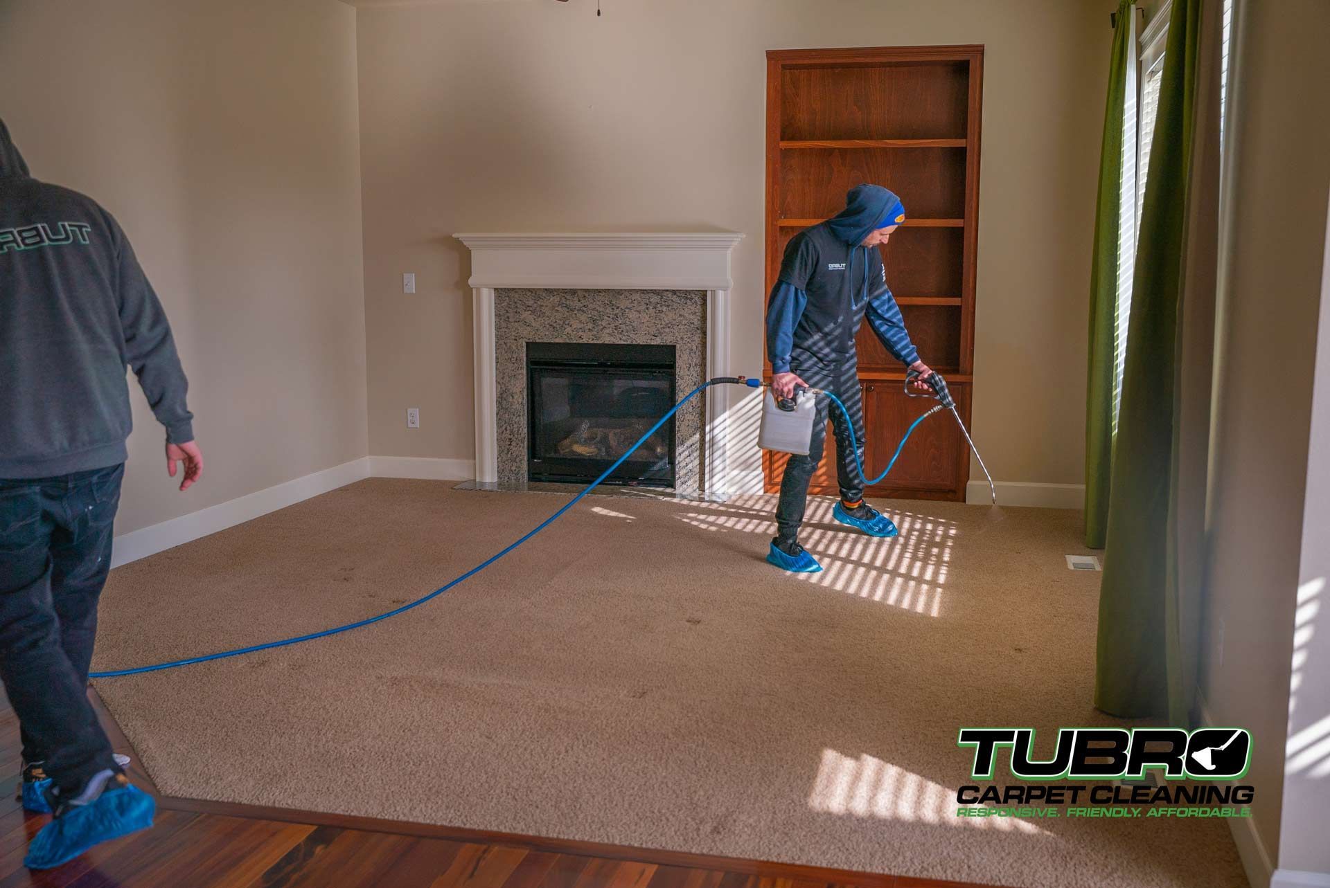 Two men are cleaning a living room carpet with a hose.