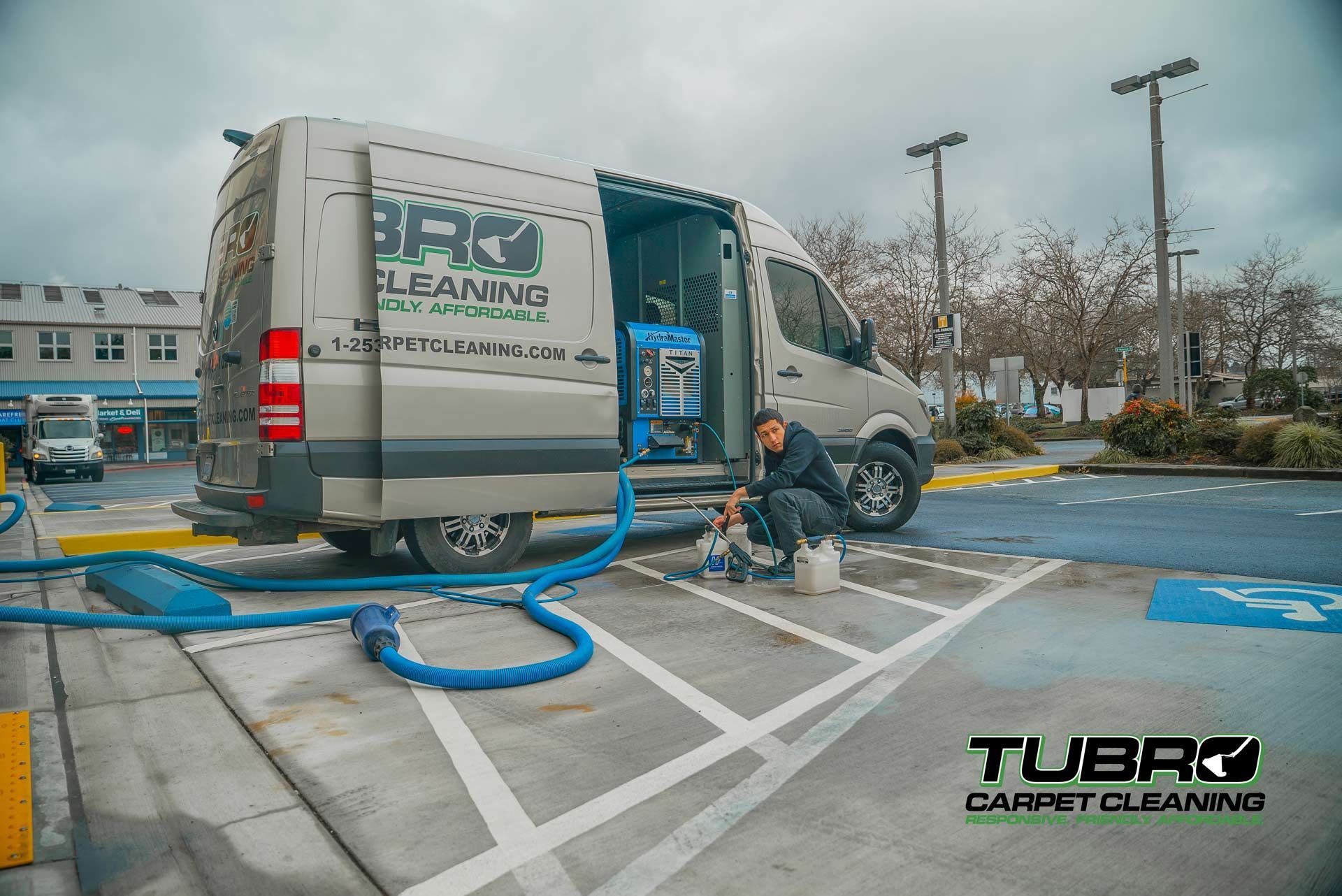 A man is kneeling in front of a carpet cleaning van in a parking lot.