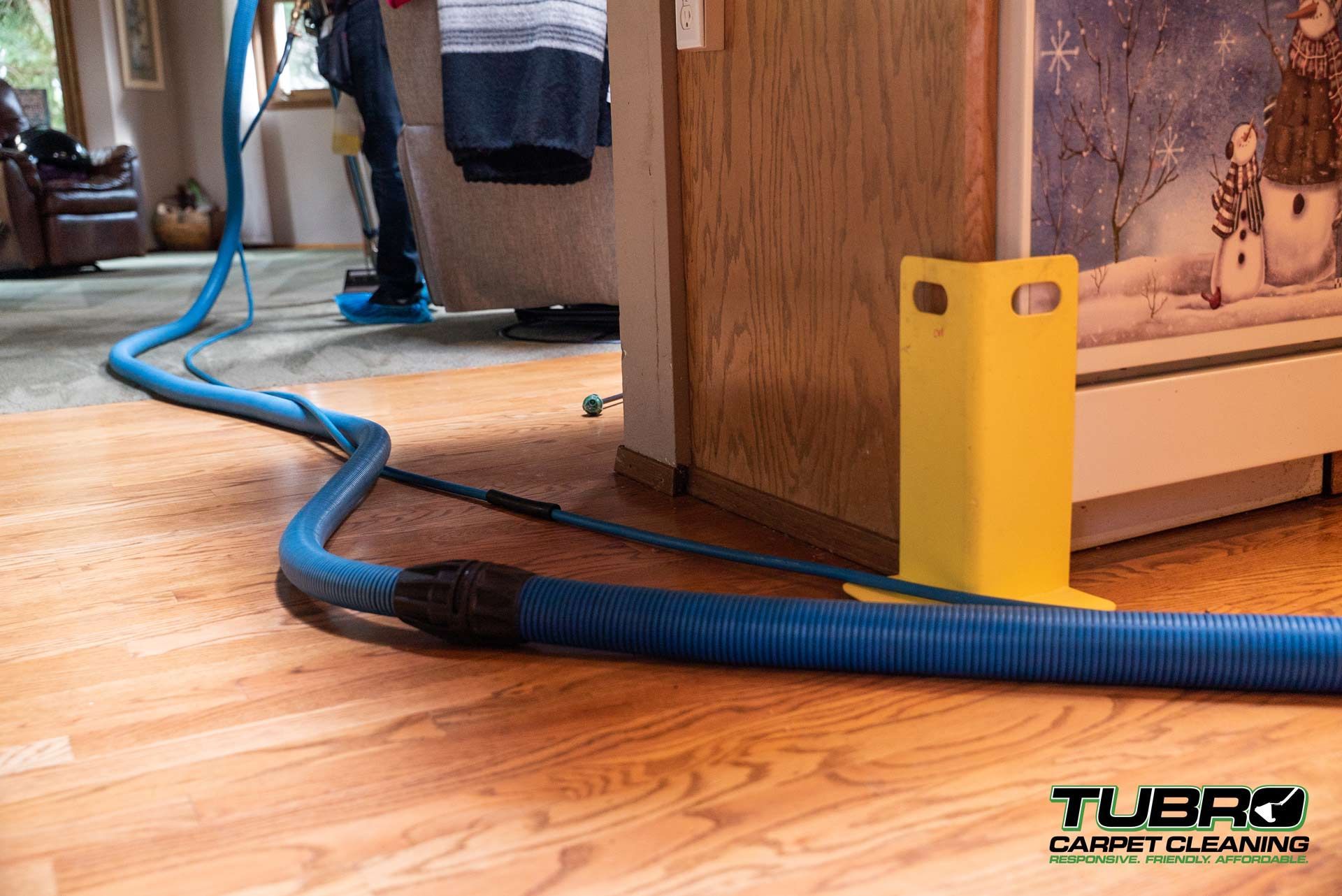 A vacuum hose is attached to a wooden floor in a living room.