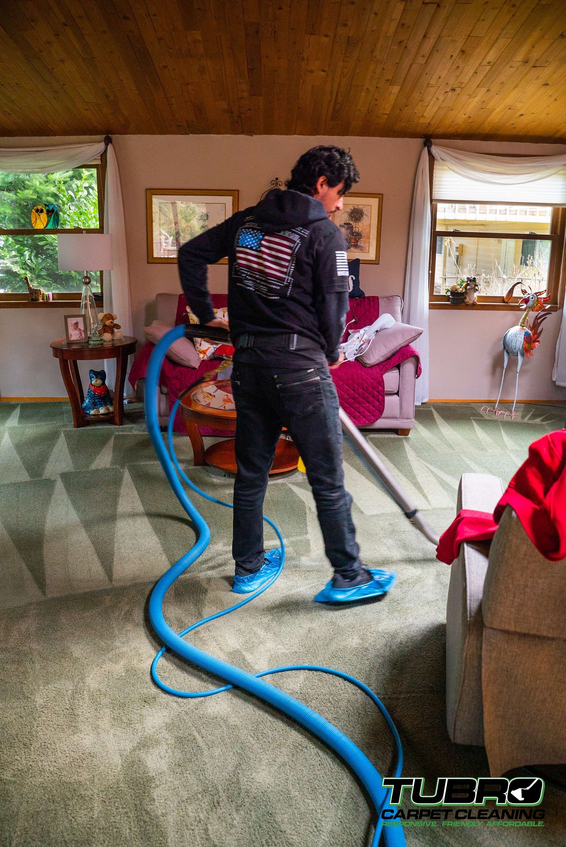 A man is cleaning a carpet in a living room with a vacuum cleaner.