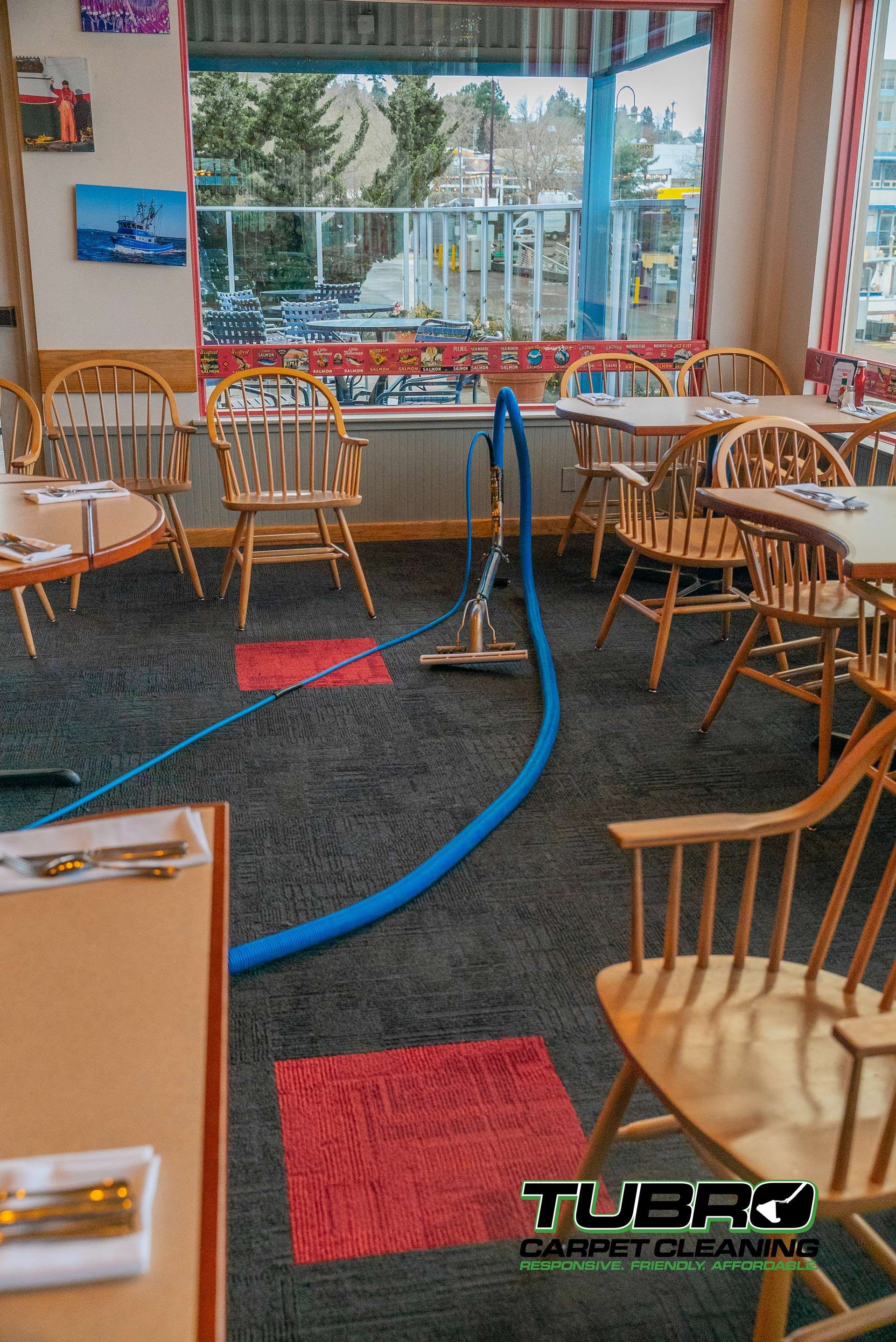 A restaurant with tables and chairs and a vacuum cleaner on the floor.
