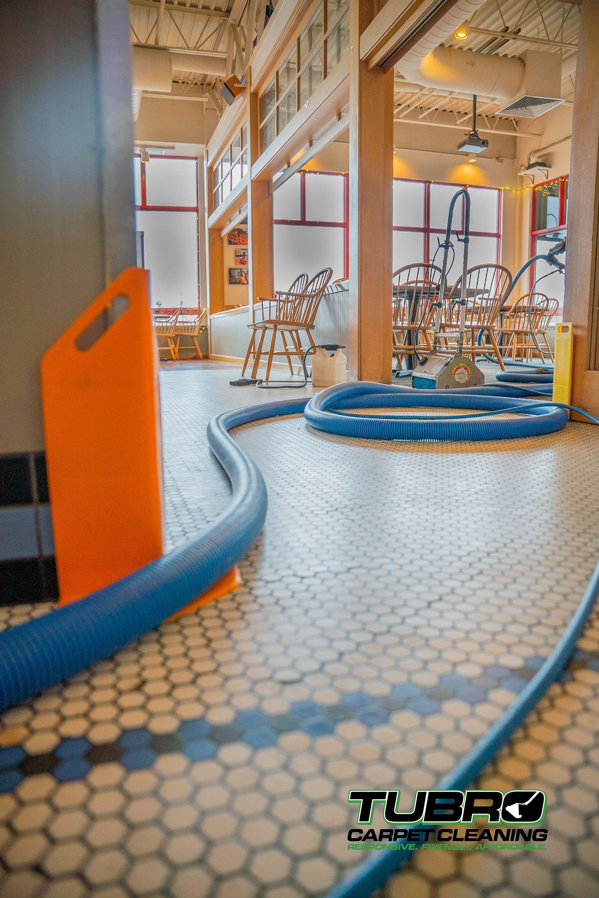 A hose is being used to clean a tiled floor in a restaurant.