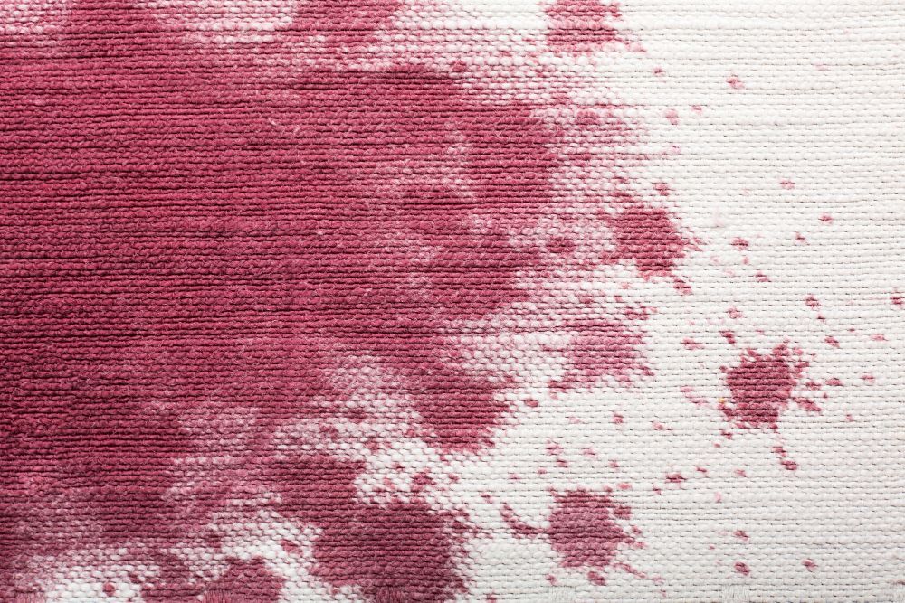 A dark red stain on a light-colored, textured fabric surface, with smaller splatters extending to the right.