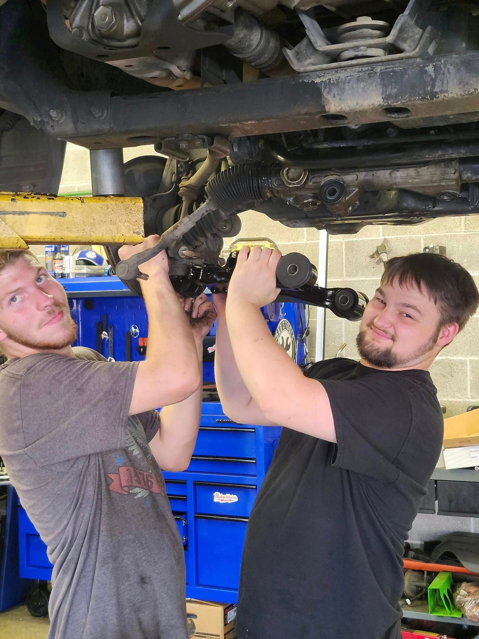 Two men are working under a car in a garage. | Oakmont Service Center