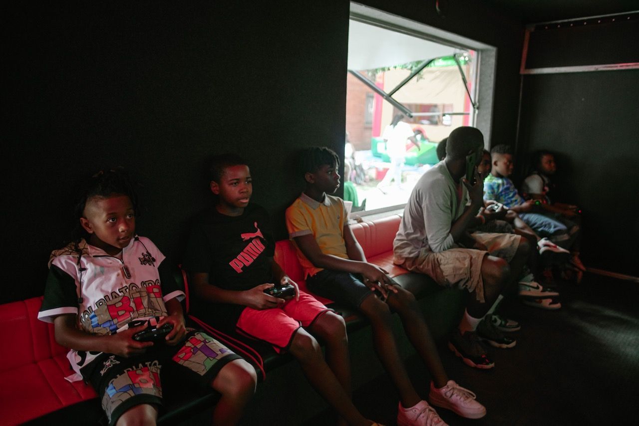 Children playing video games inside a room with a window, sitting on a bench.