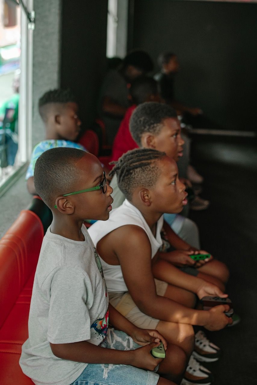 Several children seated, holding controllers, focused on playing video games in a gaming area.