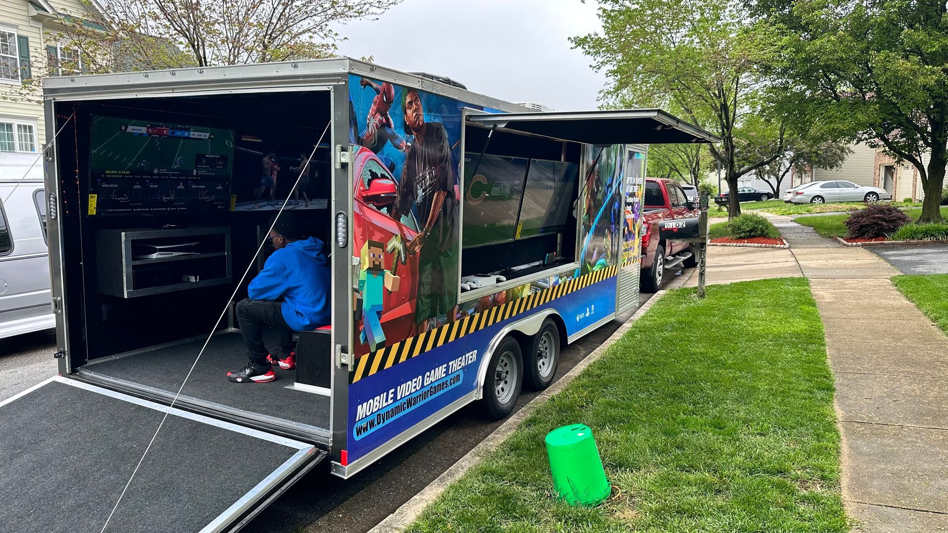 A gaming trailer parked on a lawn, with open doors. A person inside plays a game.