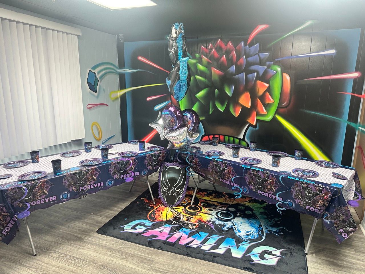 Gaming-themed party setup with tables, decorations, and a backdrop featuring a colorful controller design.