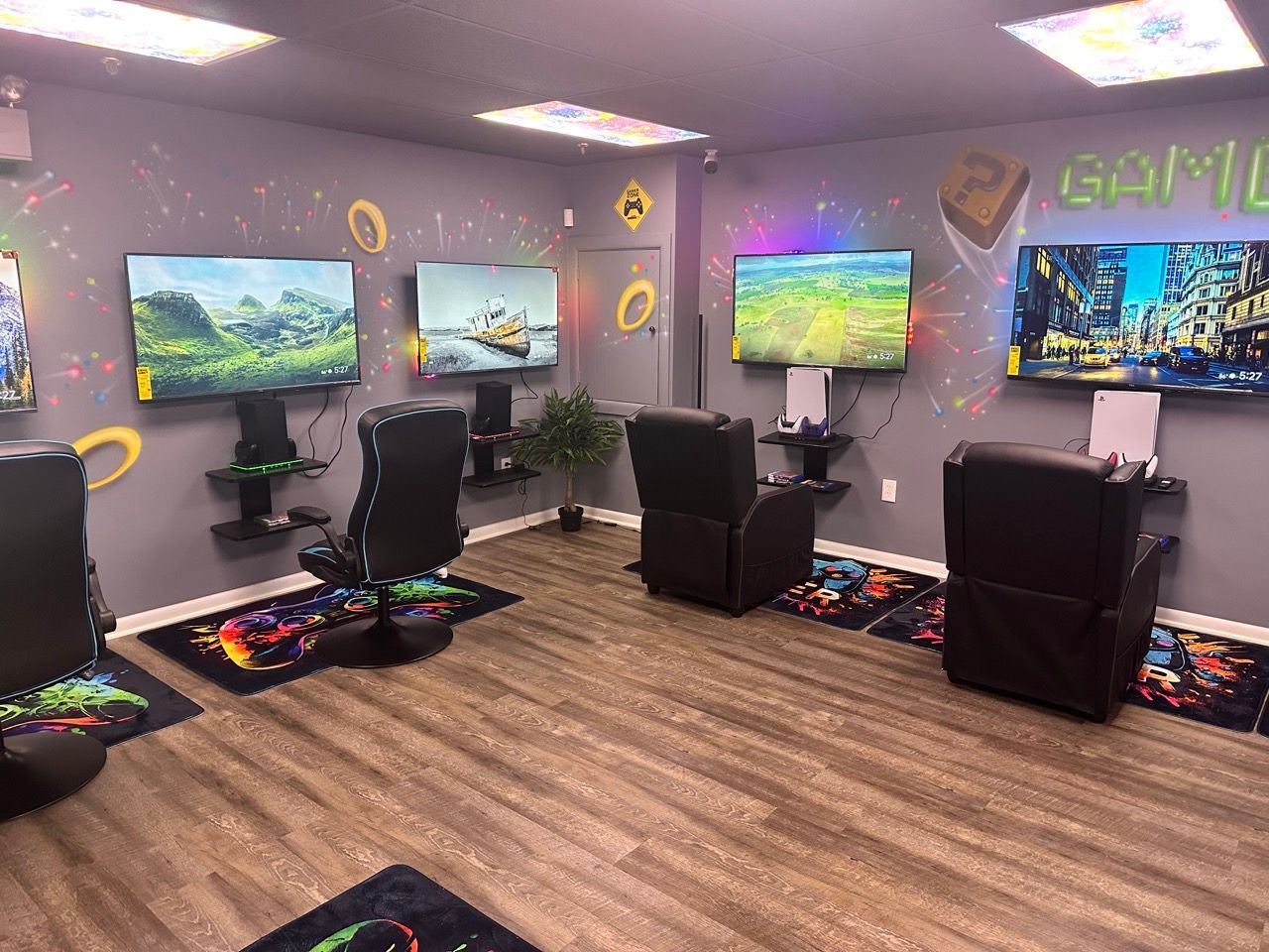 Gaming room with mounted TVs, gaming chairs, and colorful decor on gray walls.