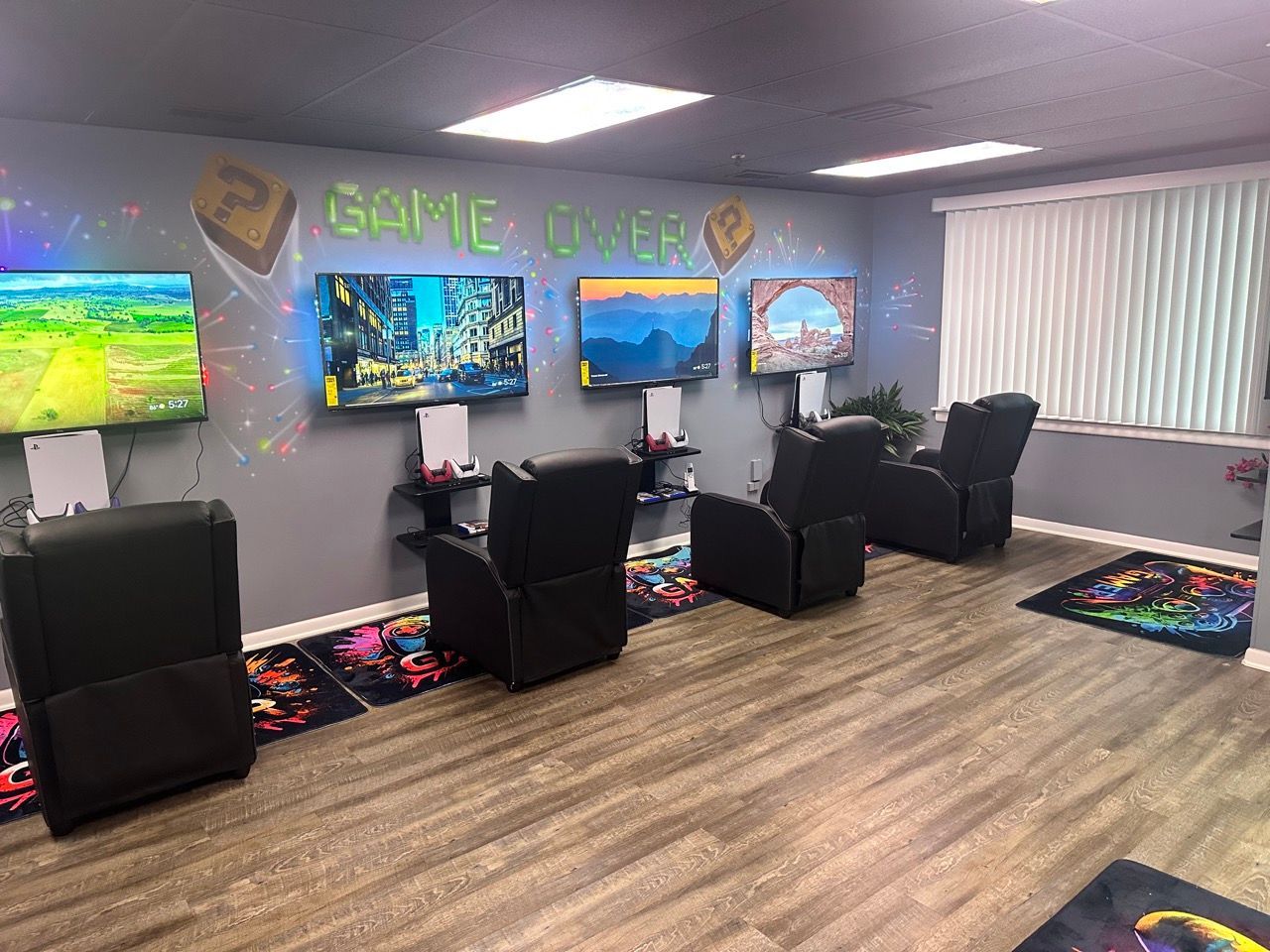 Gaming room with four TVs mounted on a gray wall, each with a black recliner. 