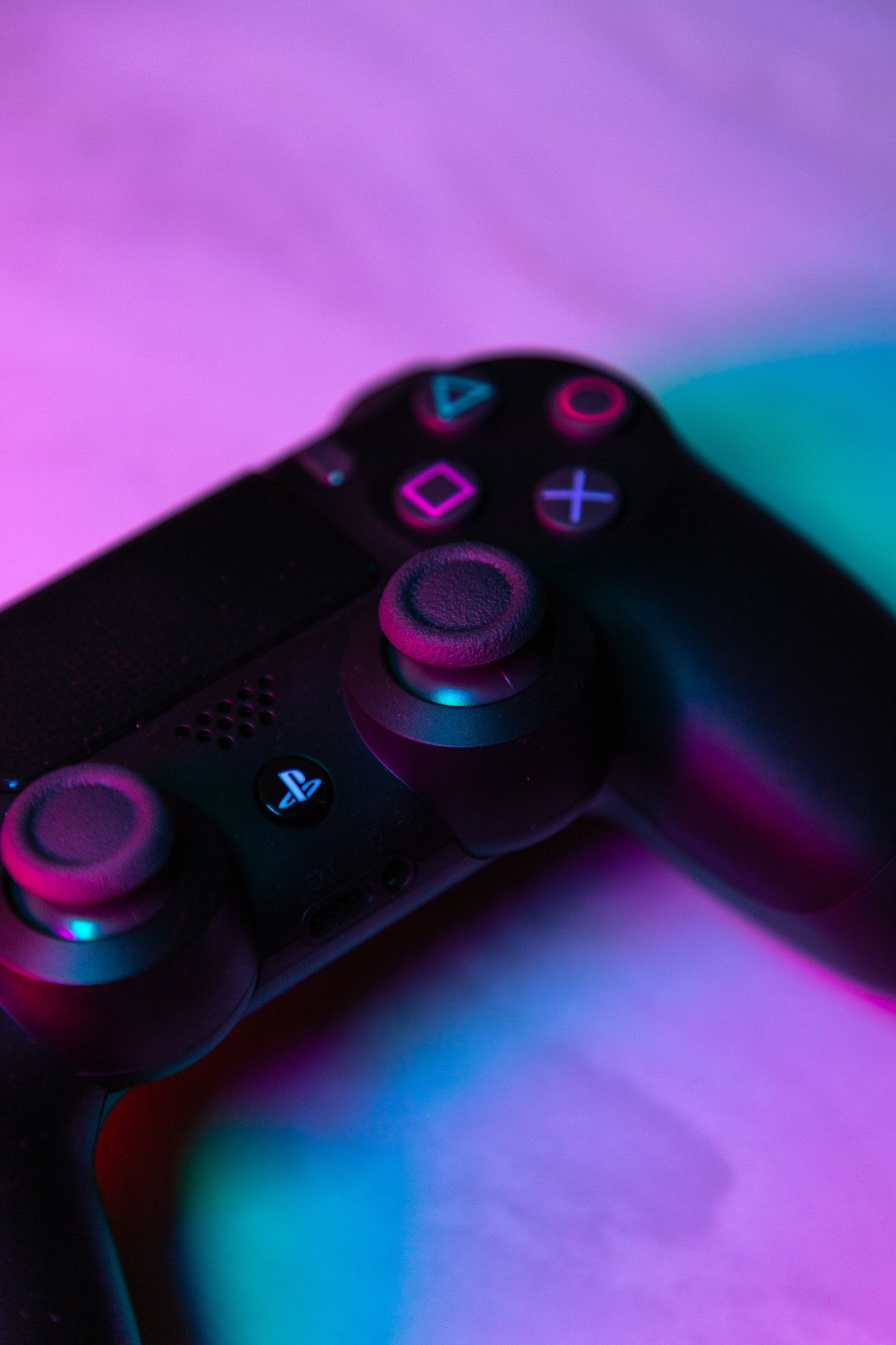 Black PlayStation 4 controller lit with pink and blue light.