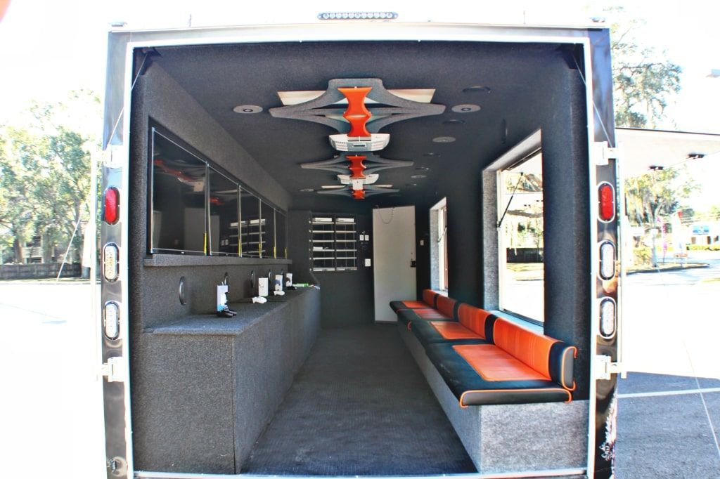 Interior of a trailer, black walls and ceiling. Orange and black seating along the right side, workstations on the left.