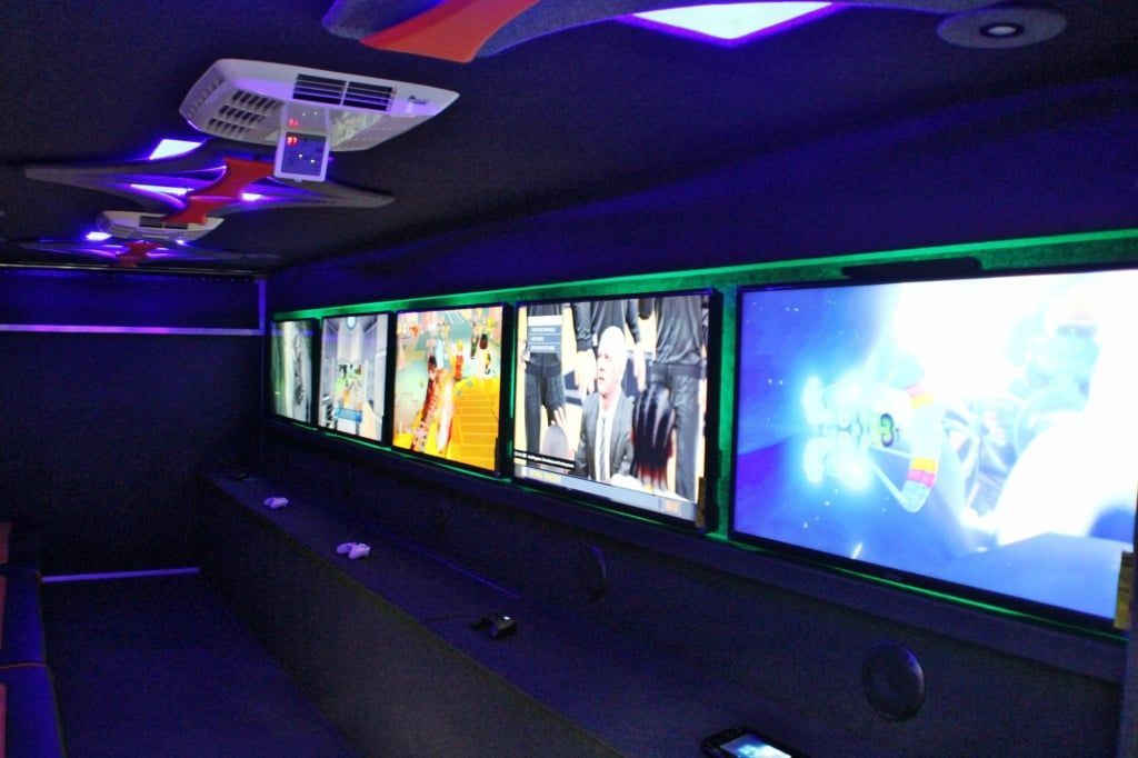Interior of a vehicle with multiple screens displaying different images, neon lighting, and dark surfaces.