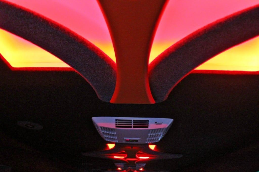Interior of a vehicle, possibly a limousine, with red and orange ambient lighting and a central air vent.