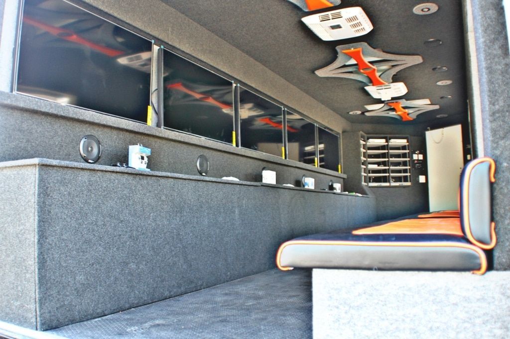 Interior of a vehicle with a long counter, multiple TVs, seating, and decorative ceiling lights.