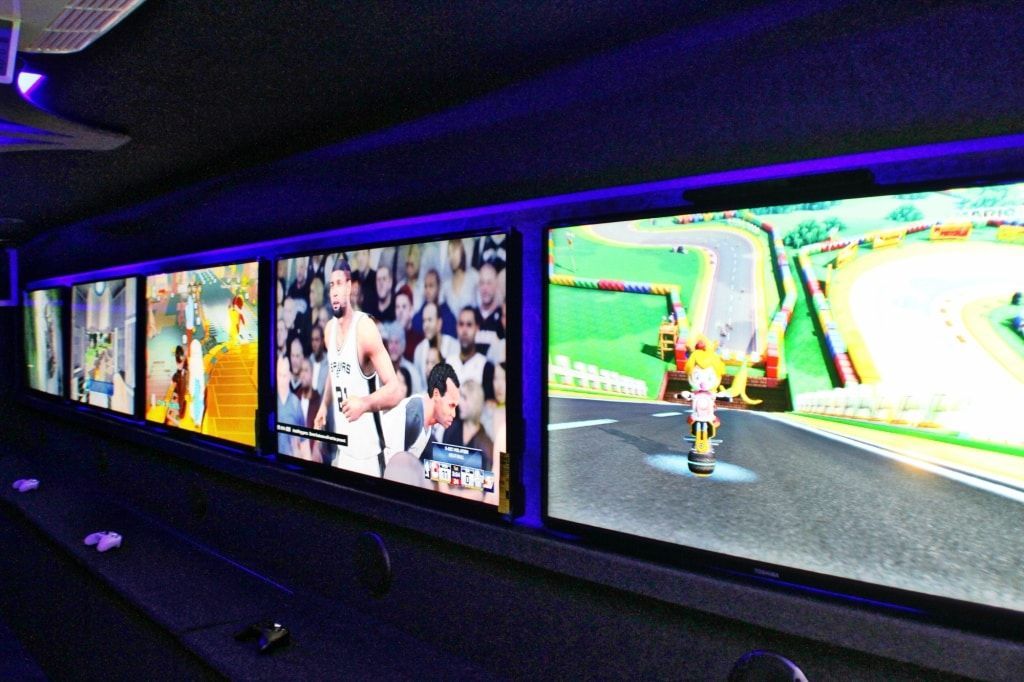 Multiple screens displaying sports and video game footage in a dark room with blue lighting.