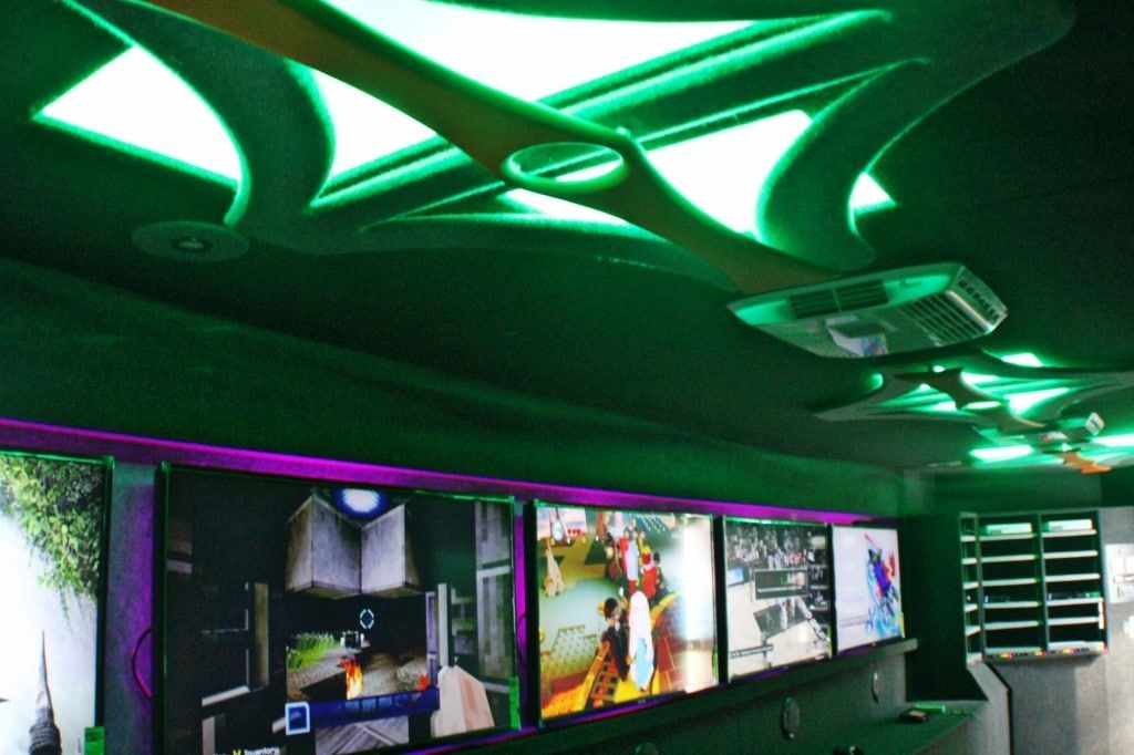 Interior of a vehicle with green neon ceiling lights and multiple screens displaying images. Purple accent lighting.
