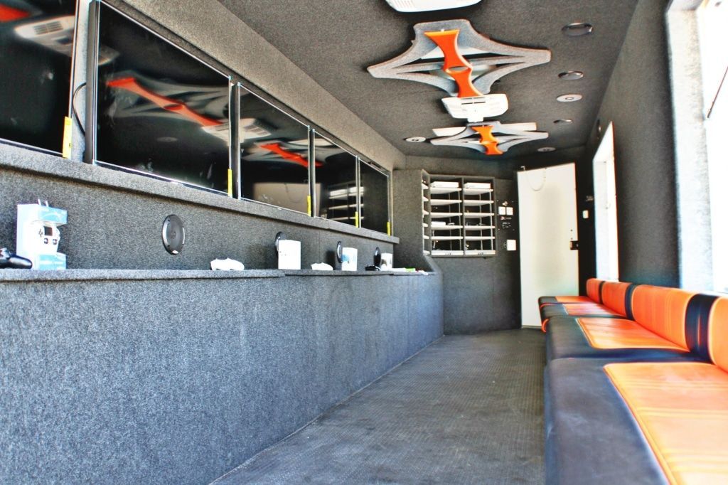 Inside a trailer: Several screens on wall, orange and black seating, dark gray interior.