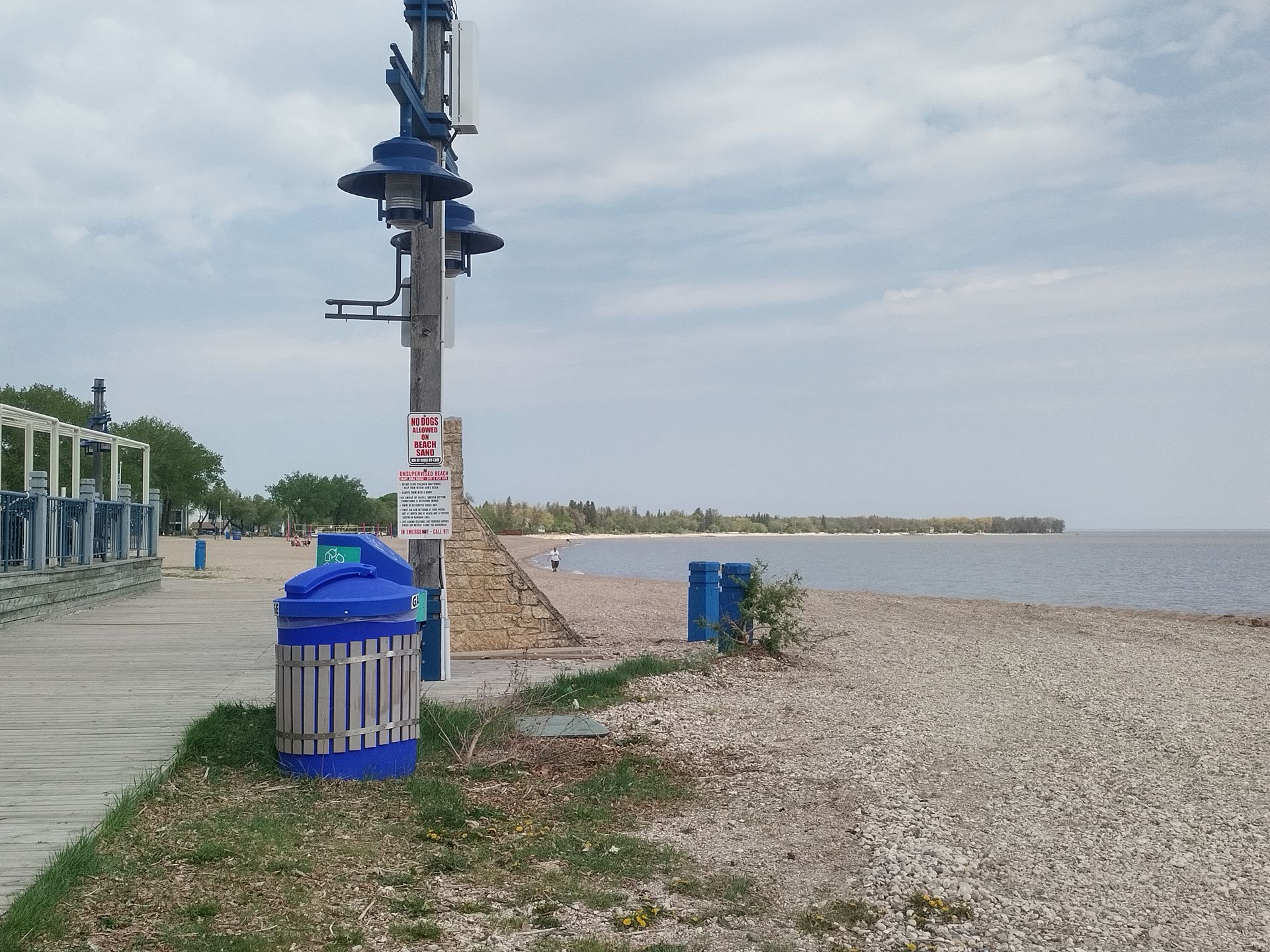 A blue trash can sits on the side of a beach