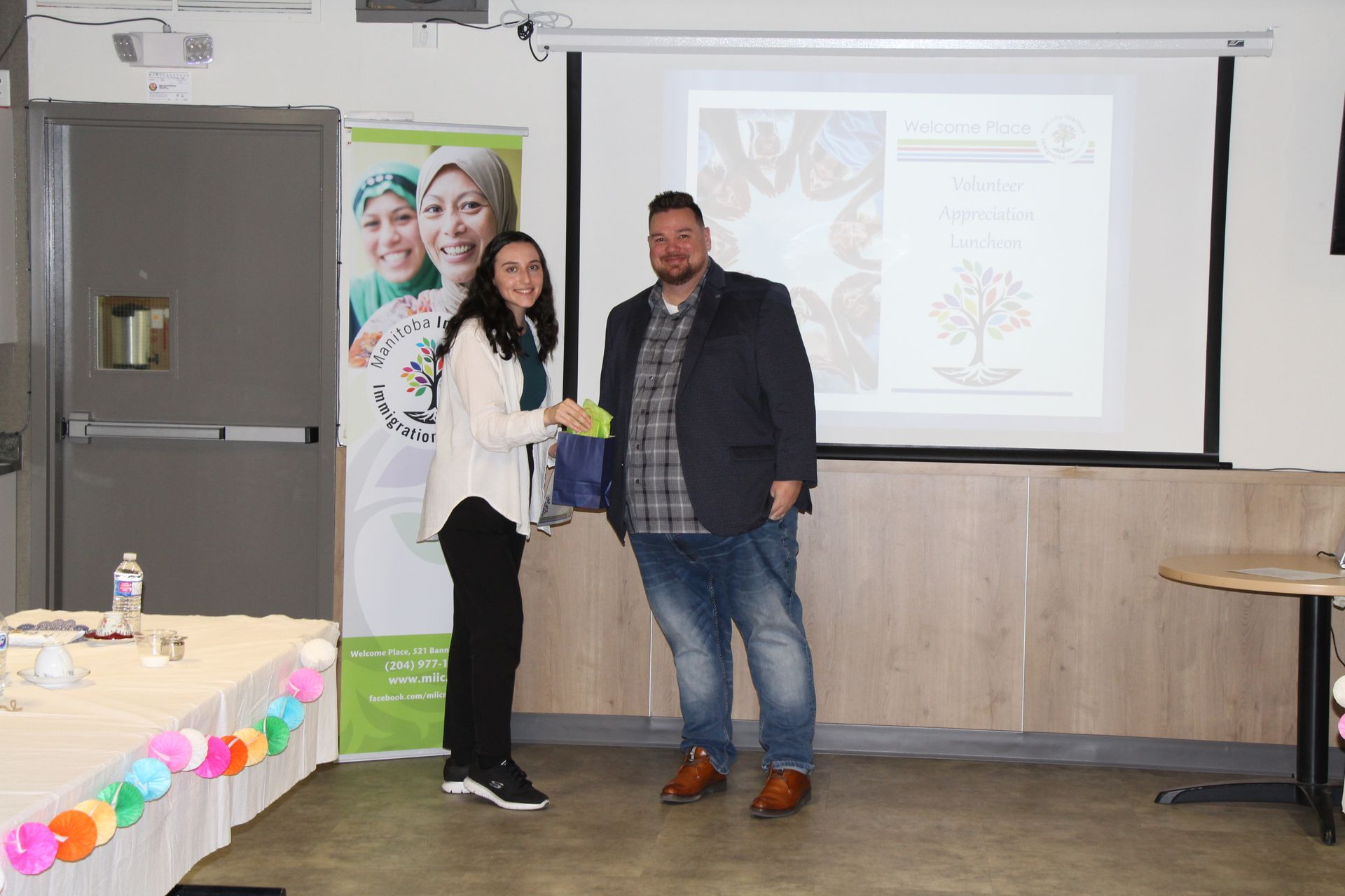 A man and a woman are standing in front of a projector screen.