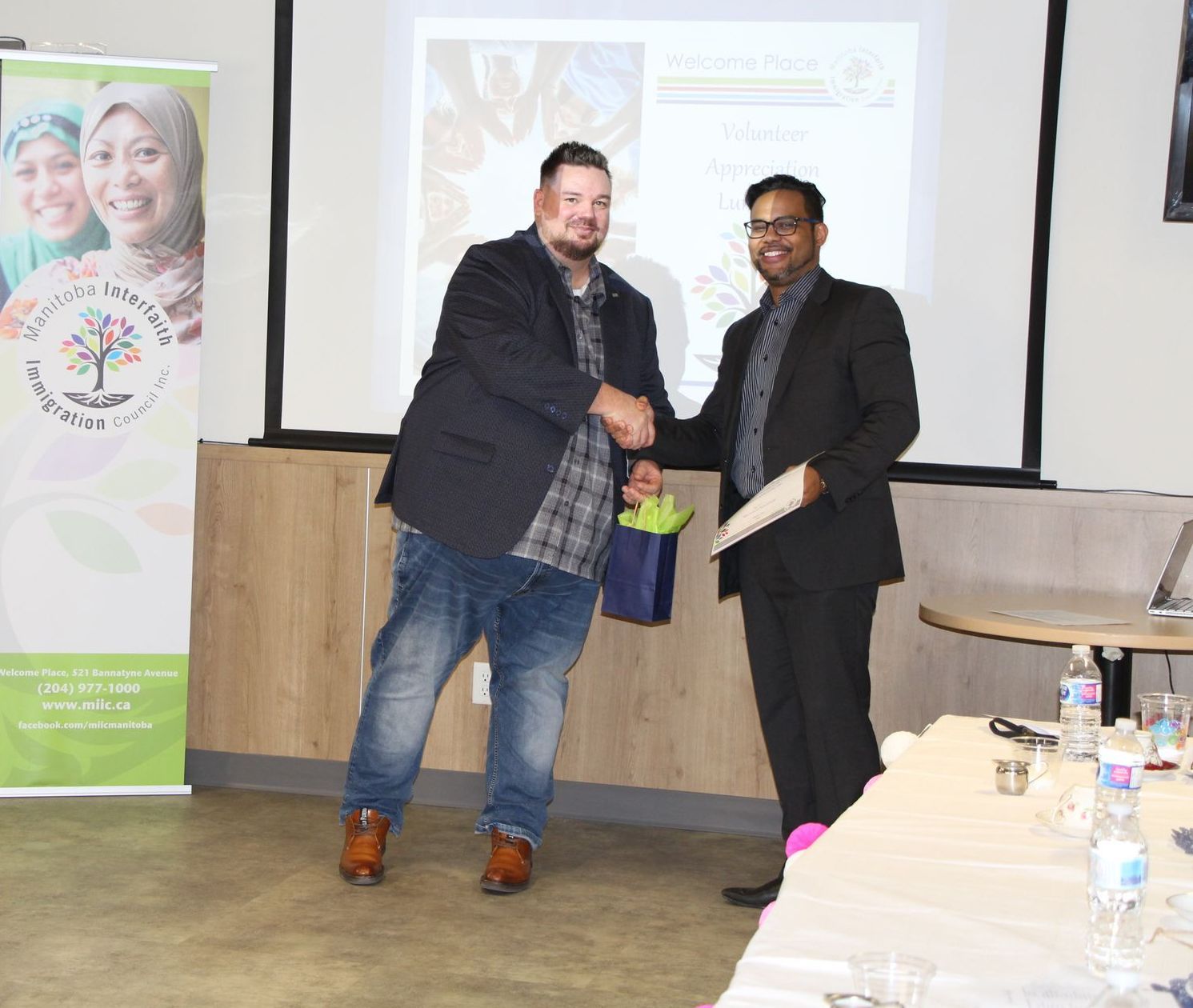 Two men are shaking hands in front of a projector screen.