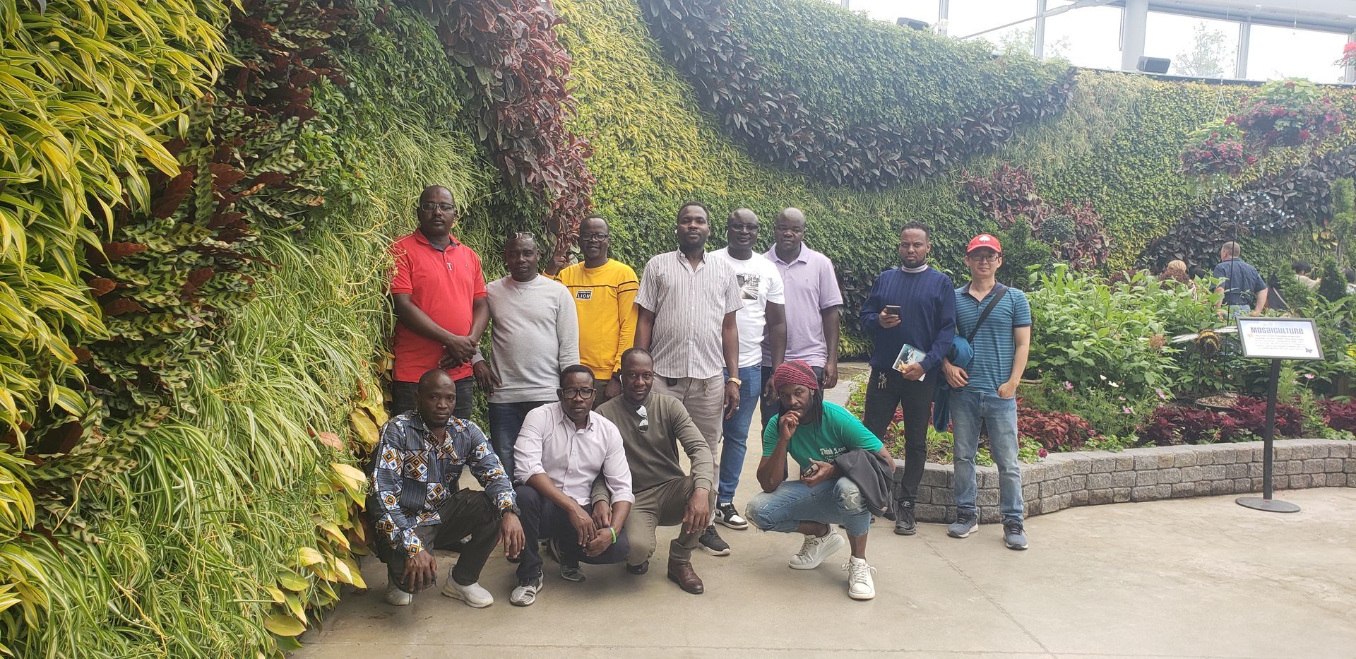 A group of people are posing for a picture in front of a wall of plants.