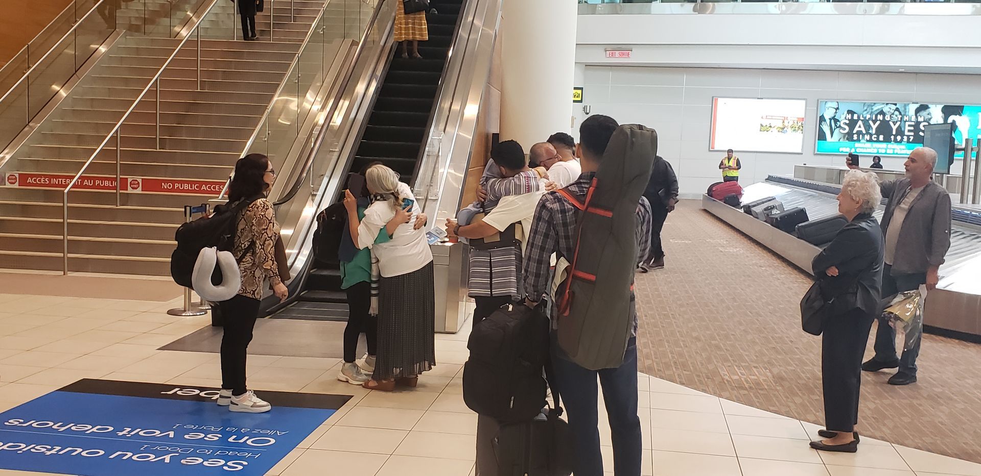 A group of people are standing in front of an escalator in an airport.