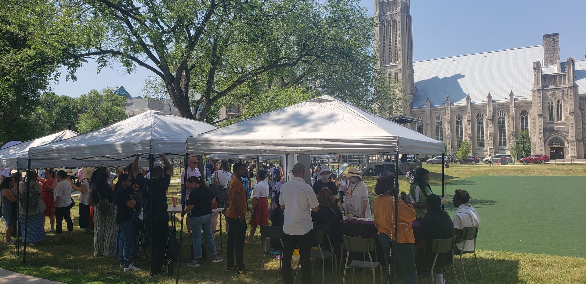 A group of people are sitting under tents in a park.