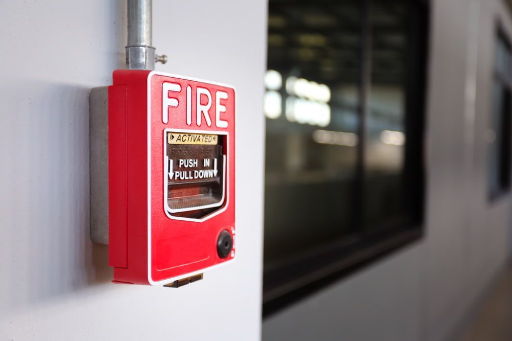 A Red Fire Alarm is Hanging on a Wall Next to a Window — East-West Fire Services In Ingham, QLD
