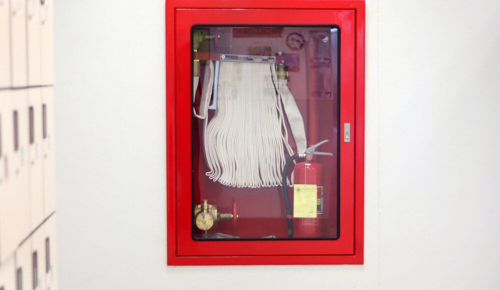 A Red Fire Extinguisher is Hanging on a Wall Next to a Fire Hose — East-West Fire Services In Bowen, QLD