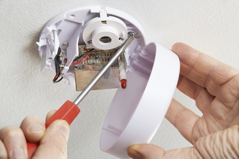 A Person is Fixing a Smoke Detector With a Screwdriver — East-West Fire Services In Ayr, QLD