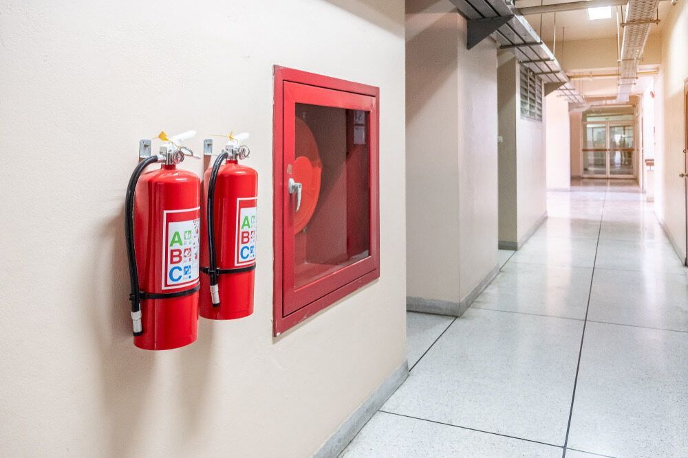 Two Fire Extinguishers Are Hanging on a Wall in a Hallway — East-West Fire Services In Proserpine, QLD