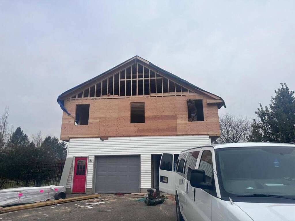 Two-story house under construction. Garage below, plywood and framing above. White van parked in front.