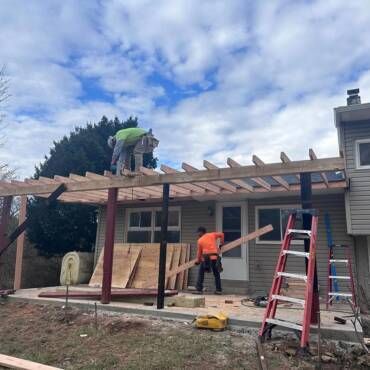 Construction workers building a pergola outside a house. Blue sky.