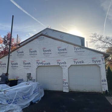 Garage under construction, covered in Tyvek wrap; cloudy sky.