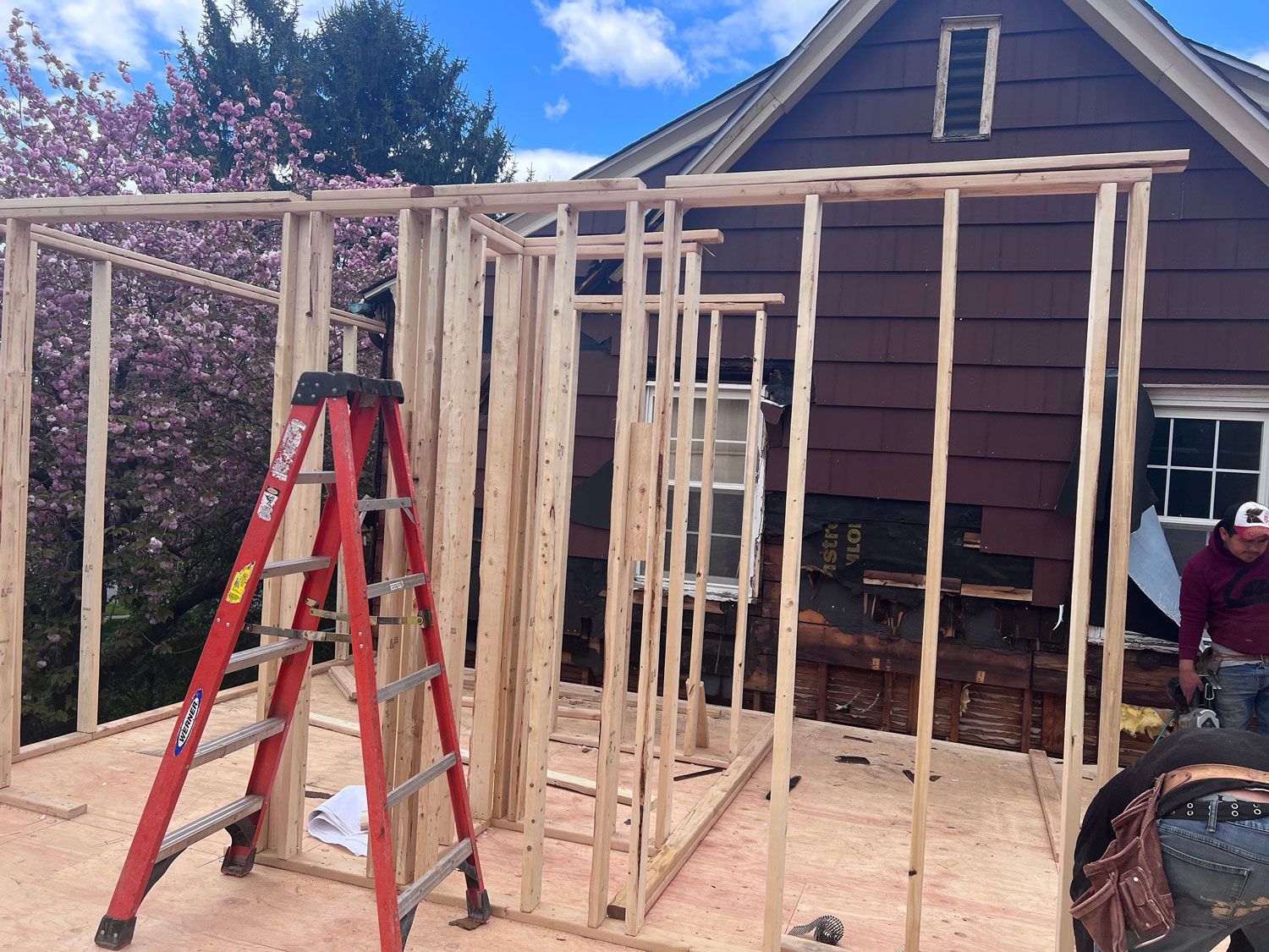 Construction of a wooden frame addition to a brown house; a red ladder stands nearby.