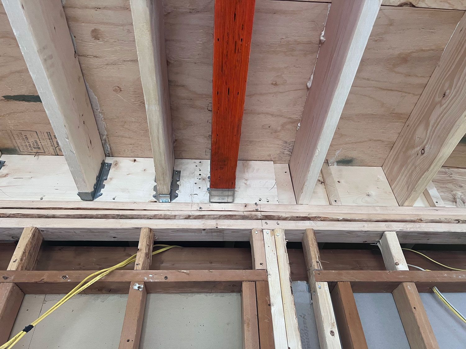 Wooden framing of a wall and ceiling during construction, featuring a painted orange support beam.