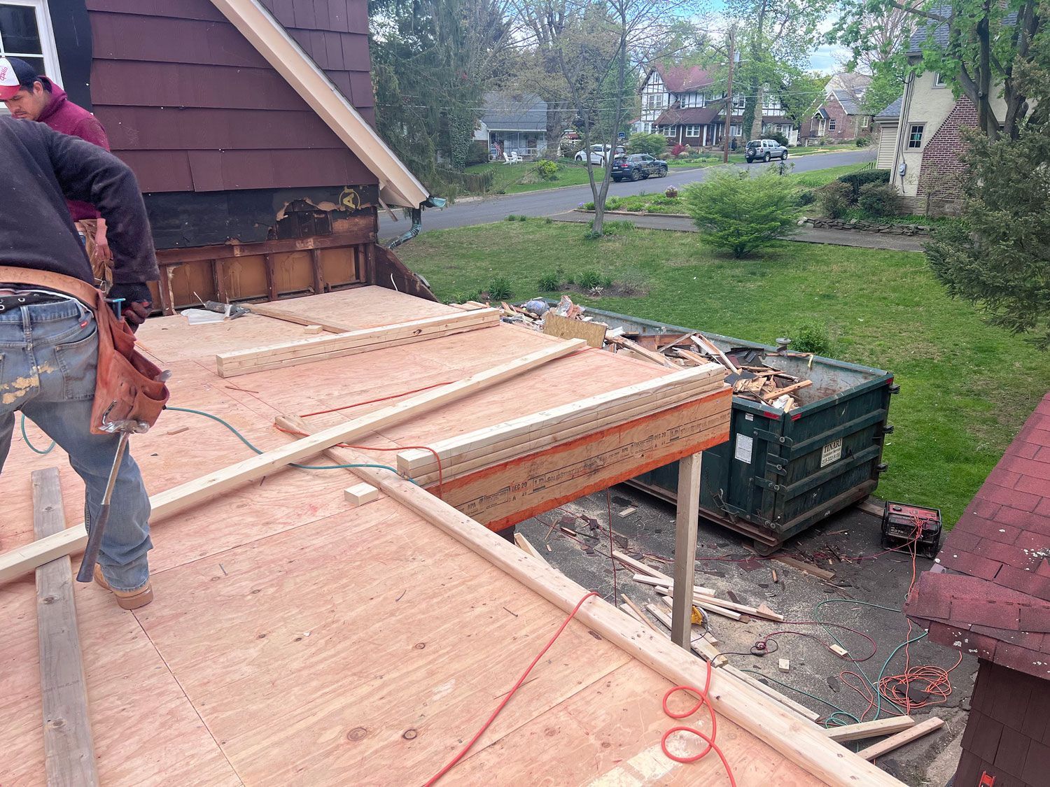 Construction workers on a roof, installing plywood. Sunny day, residential neighborhood.