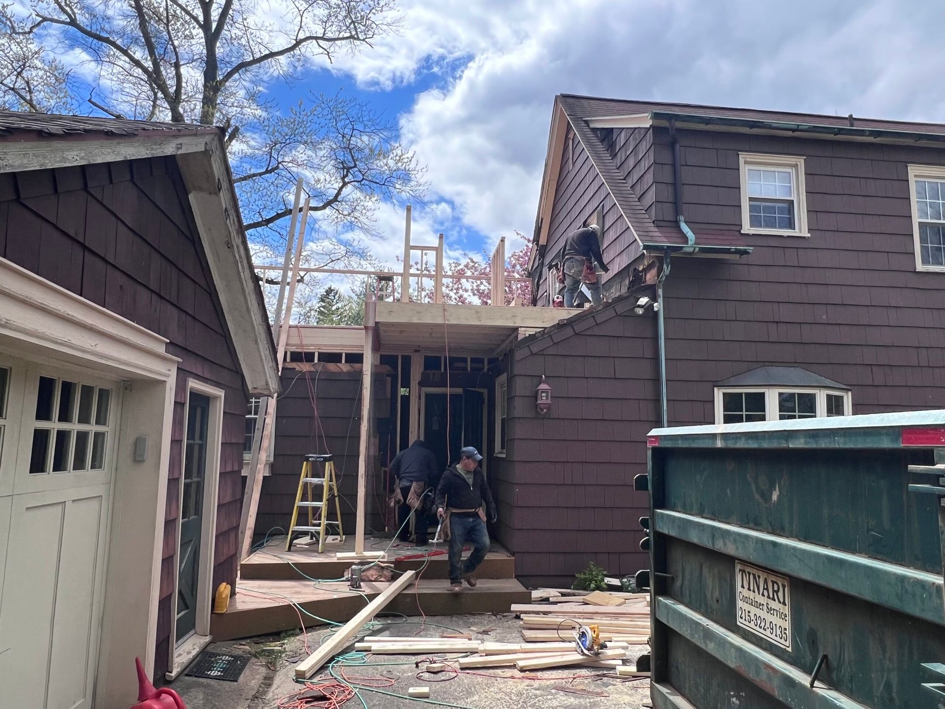 Construction workers build an addition to a brown house, with garage on the left.