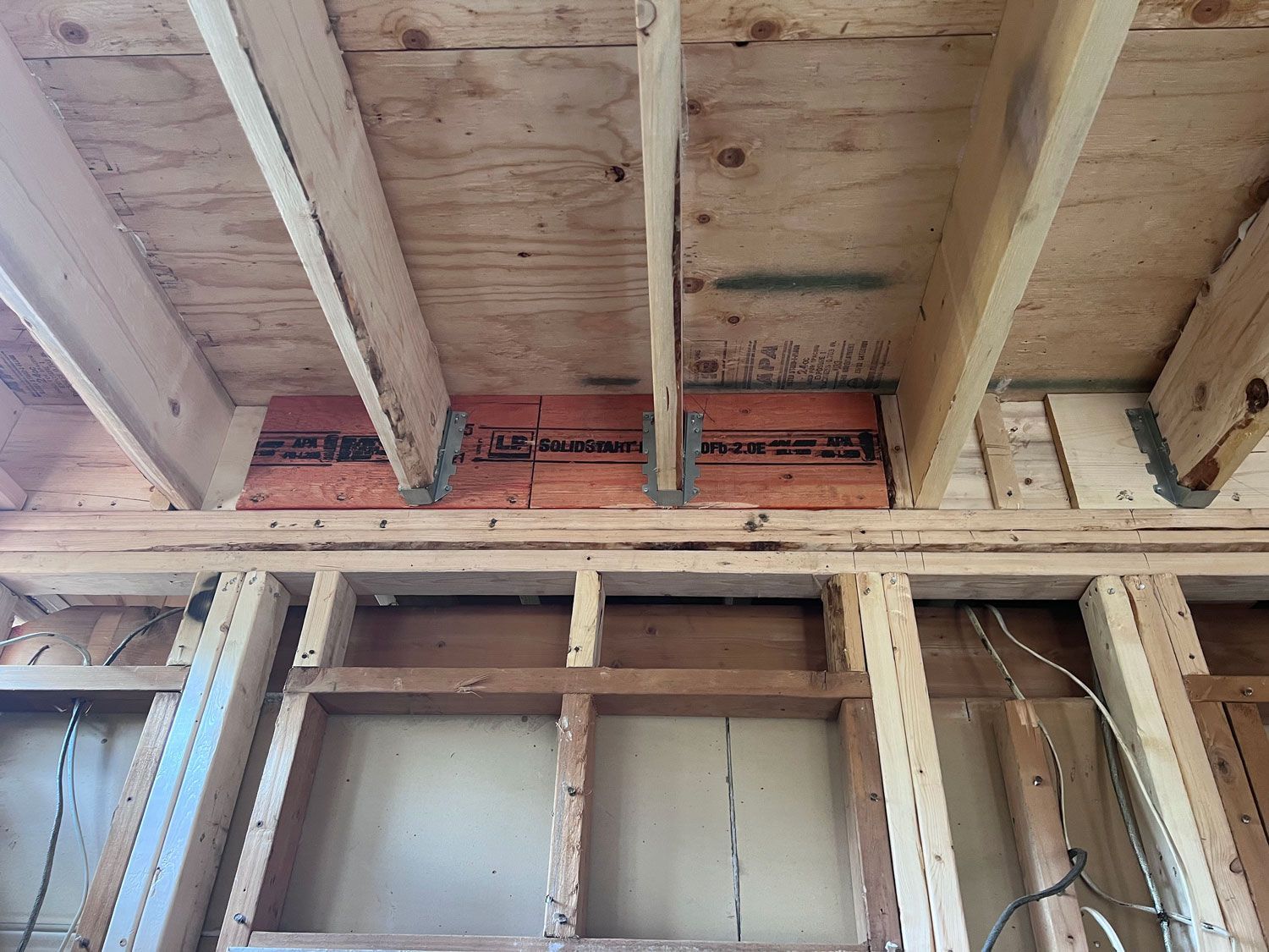 Interior framing of a structure with exposed wood beams, plywood ceiling, and orange insulation.