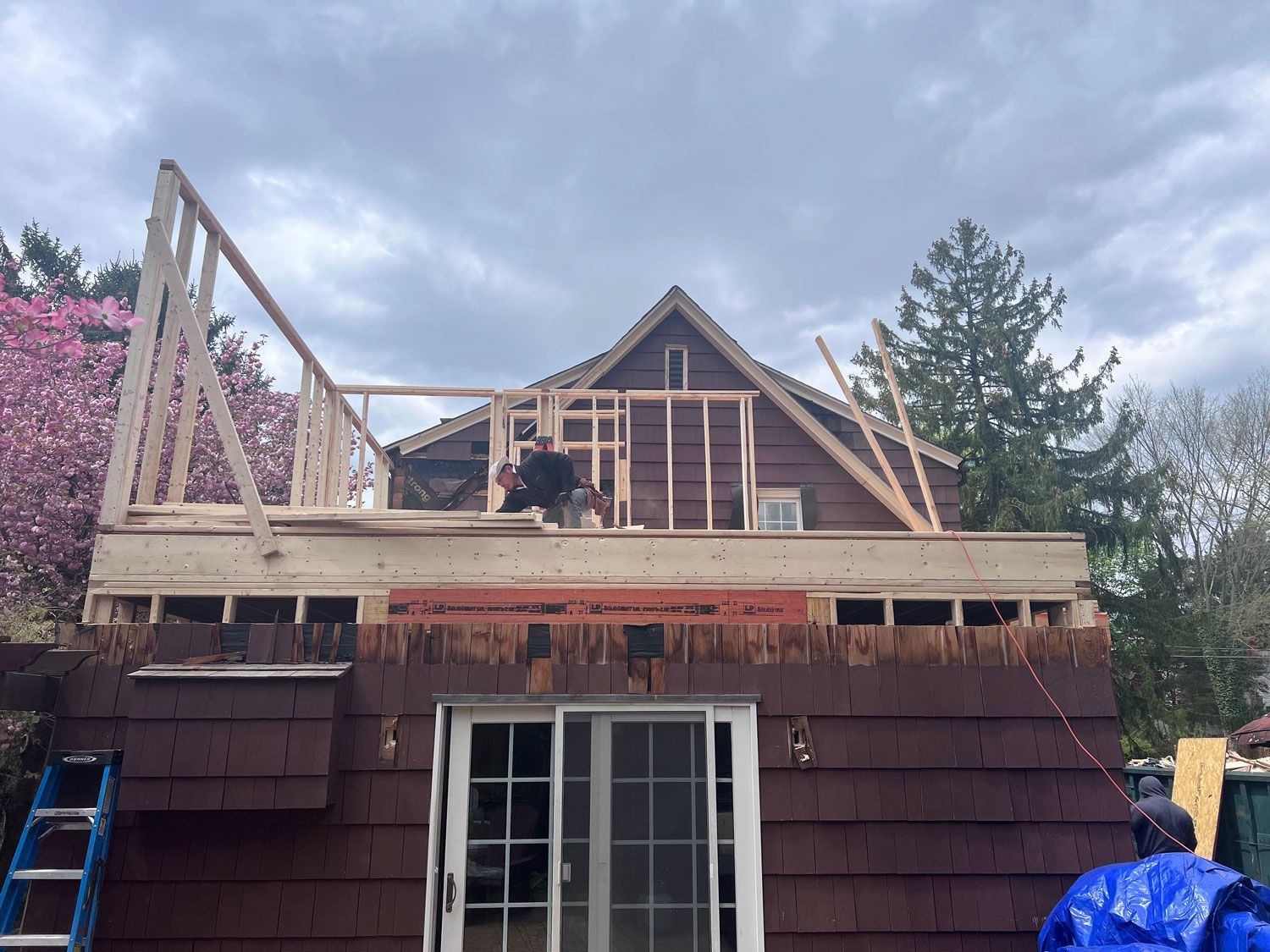 Construction site: Worker framing the roof of a house, brown siding, cloudy sky.