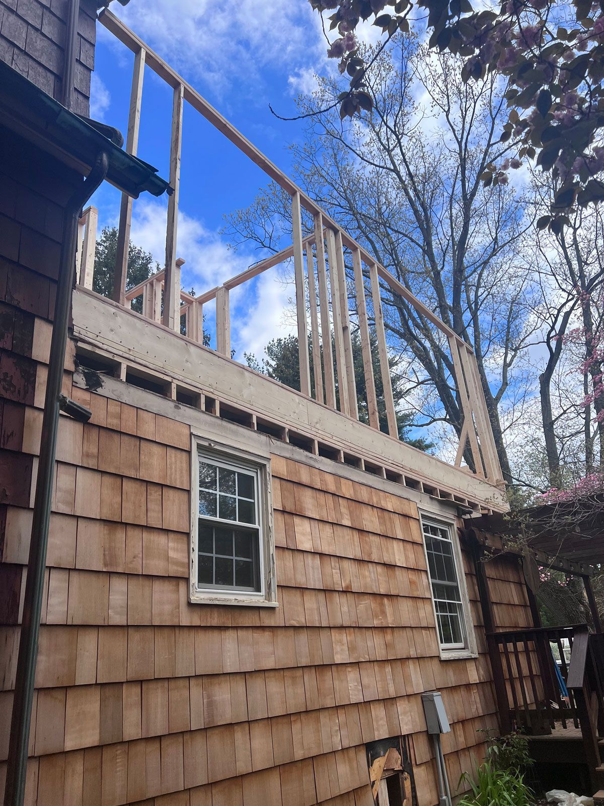Construction of a second story on a wood-shingled house, against a blue sky.